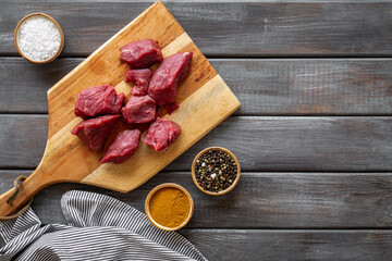 Raw beef meat cutting into pieces on wooden board with spices