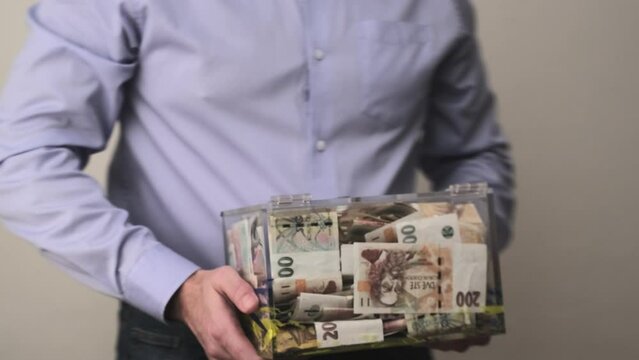 Man gave a transparent donation box full of money. CZK czech koruna banknotes. A Charity financial support, collects money for a noble cause. The act of giving supports charitable initiatives.