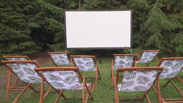 A movie theater in nature with folding chairs arranged in front of a large screen. outdoors mobile cinema Outdoor leisure