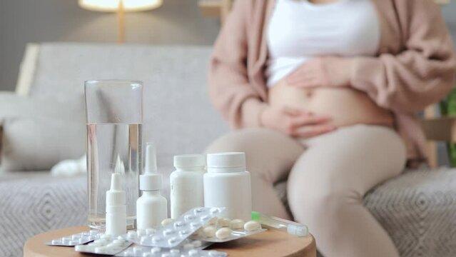 Unrecognizable unknown unwell pregnant woman sitting on sofa at home female suffering virus grippe touching stroking her bare belly treating grippe at home