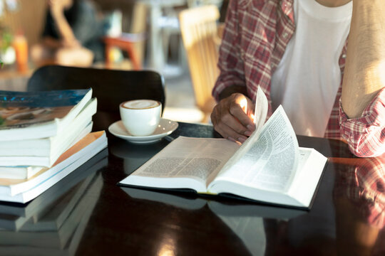Close-up of young man's hand reading a book with cup of coffee while sitting in coffee shop.