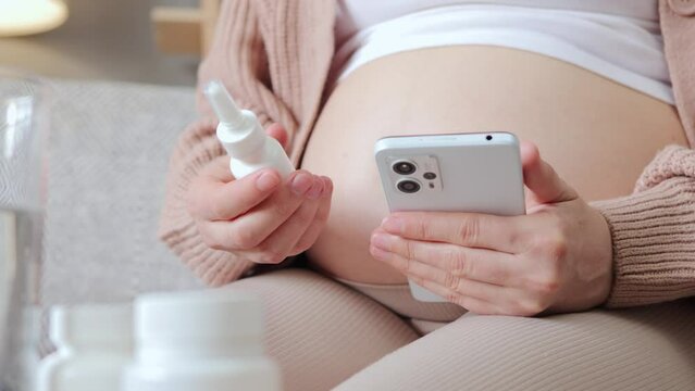 Anonymous unrecognizable sick pregnant woman holding nasal checking smartphone searching information about harm from nasal drops when used during pregnancy