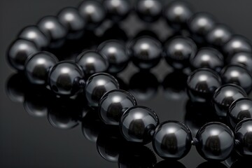 A close-up of a black pearl necklace on a dark reflective surface