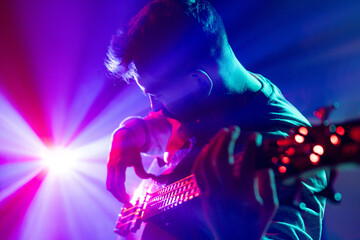 Portrait of young man performing playing chords electric guitar in neon light and visible smoke on stage. Rock and roll. Concept of rock and classic music, hobby and work, energy, music festivals. Ad