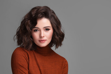 Fototapeta premium Portrait of beautiful young woman with wavy hairstyle on grey background. Space for text