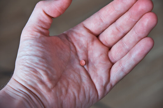A blood-thinning pill lies on a man's palm. Prevention of blood clot formation. Close-up.