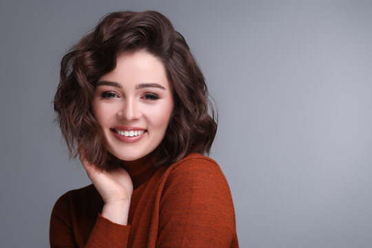 Portrait of beautiful young woman with wavy hairstyle on grey background