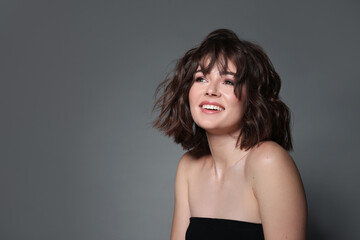 Fototapeta premium Portrait of beautiful young woman with wavy hairstyle on grey background. Space for text
