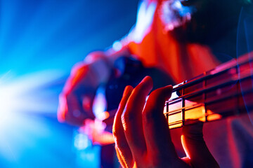 Bassist's hands playing melodic chords of new track in action with colorful concert light flare in...