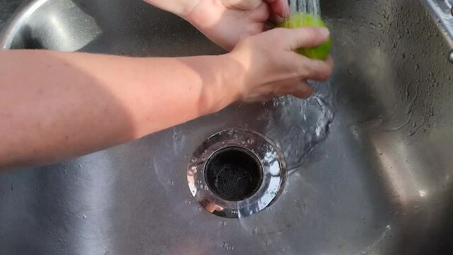 Unas manos de mujer lavando una  naranja  con   agua  en un fregadero
