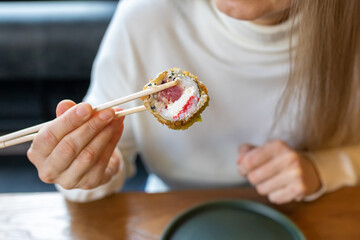 A woman's hand holds a sushi roll with chopsticks. Everyday food. An ordinary raw photo.
