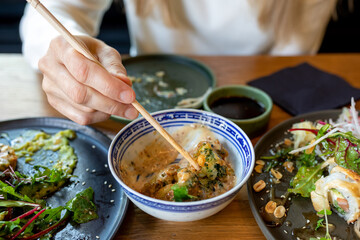 Lunch process. Womans hand takes out Asian traditional food with chopsticks. Everyday food. Mess on...