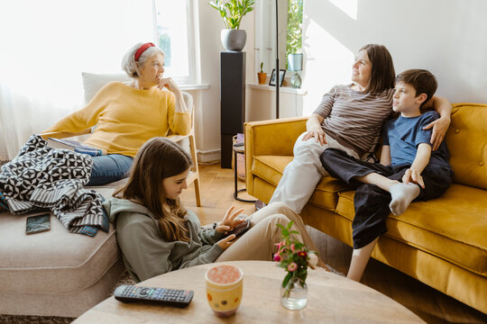Mother and son talking with senior woman sitting on chair at home
