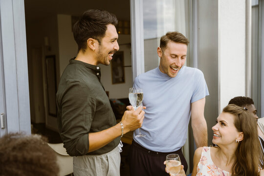 Happy male friends enjoying drinks with female friend at dinner party in balcony