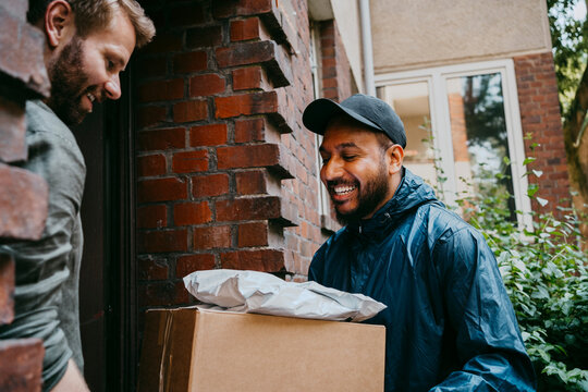 Smiling courier delivery person talking with man while delivering packages at doorstep