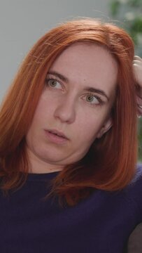 Distressed woman tries to find interesting TV program to watch at home after work. Redhead housewife leans head on hand holding remote control closeup