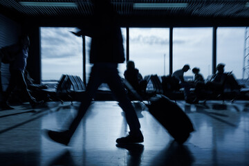 Passenger with luggage walking along an empty airport departure lounge, handheld motion blur shot....