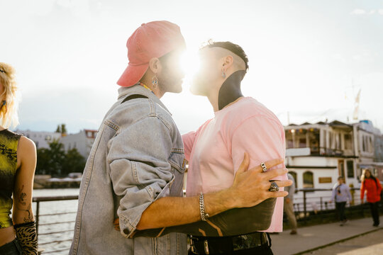 Side view of romantic gay man kissing non-binary friend on promenade