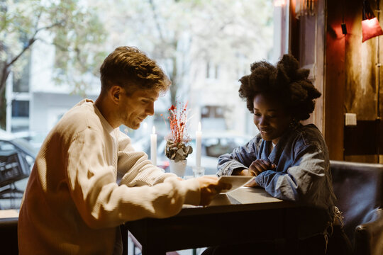 Multiracial couple going through menu card while sitting at table during date at bar