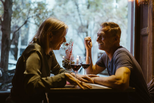Happy man flirting with woman while sitting with wineglasses on table during date at bar