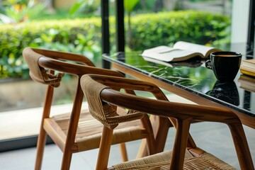 Close up photo of two wooden chairs with woven rope seats at a black marble table, with coffee and a book on the table, a window in the background, a modern architecture interior design - obrazy, fototapety, plakaty