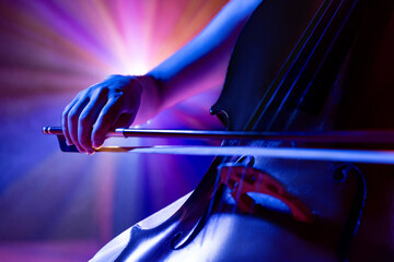 Close up photo of skilled musician, cellist performing symphony in purple-blue spotlights on stage...