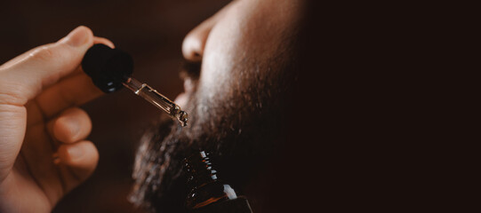 Barber applies for growth beard oil with dropper for man in barbershop. Concept spa cosmetic and...