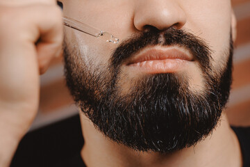 Barber applies for growth beard oil with dropper for man in barbershop. Concept spa cosmetic and...