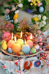Burning candles in shape of colorful eggs and flowers on plate. festive spring season. table decor...