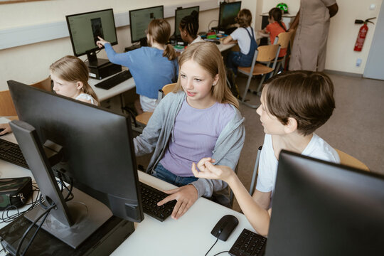 High angle view of male and female classmates discussing while sitting in computer class at school