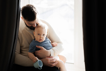 Father hugs baby boy, young man kisses his son on head in living room. Concept lifestyle in home,...