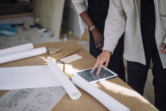Midsection of female constructor engineer explaining blueprint to colleague over digital tablet on table at under constr