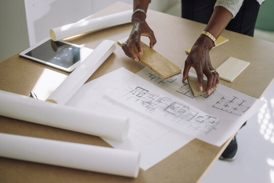 Mature female architect preparing designs modules over blueprint while working at under construction apartment