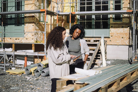Female construction engineer discussing with client over digital table while standing in front of under construction apa