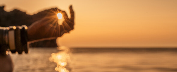 Banner. In blur closeup the hand of a young woman in bracelets. Practicing yoga on the beach with sunset. Keeps fingers connected, the sun shines through them. The concept of a healthy lifestyle