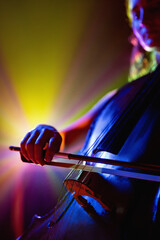 Cropped portrait of talented young woman, musician, cellist performing symphony in purple-yellow spotlights. Selective focus. Concept of hobby and work, music festivals, concerts, symphony, culture.