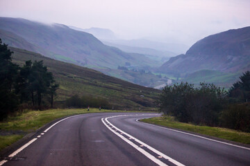 Road descending down into a mysterious misty valley in Eryri National Park in Wales