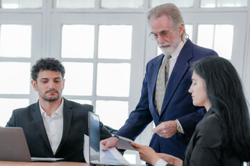 Fototapeta premium Corporate business team and manager in meeting. Diversity of business people of African and Latin women and Caucasian men are working together. Senior boss are consulting team at clean interior room.