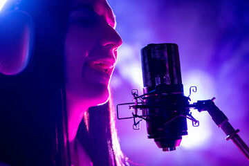 Close up portrait of music artist singing into condenser microphone, illuminated by vibrant spotlights on stage with smoke. Concept of art, work and hobby, music festivals, self expression, concert.