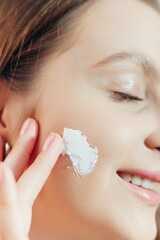 Beautiful young woman applying cream on the cheek. Face Skin care concept