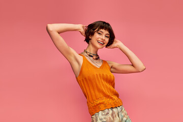 happy young woman with short brunette hair in vibrant summer attire laughing on pink backdrop