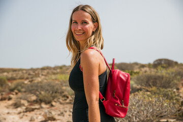 A woman is smiling and wearing a red backpack in the nature