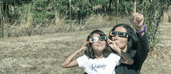 Mother and daughter, family viewing solar eclipse with special glasses in a park