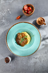 Braised beef cheeks with creamy mashed potatoes on blue rimmed ceramic plate, garnished with microgreens