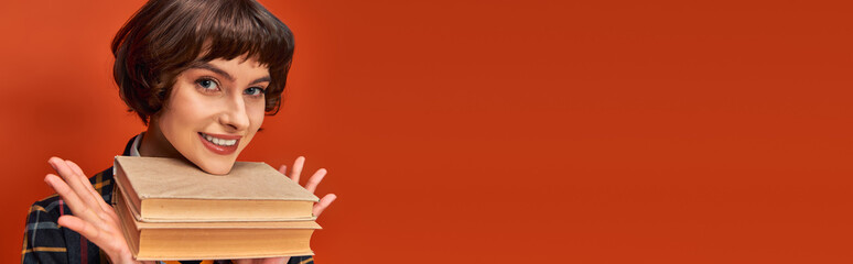 banner of smiling college girl in uniform holding books near chin on orange background, knowledge