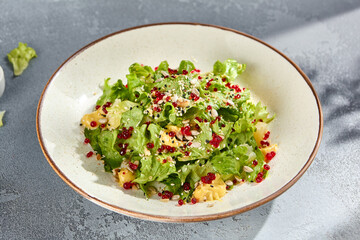Green salad with pineapple chunks and pomegranate seeds, fresh and colorful in a speckled bowl