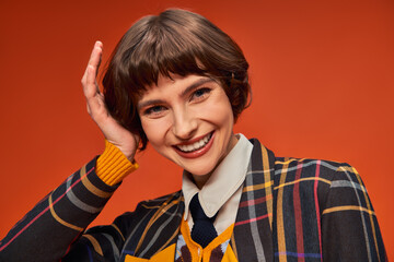 happy college girl with short hair posing in her uniform on orange background, high school