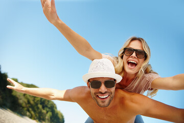 Couple, sunglasses and piggyback on vacation, fun and peace at beach or game by blue sky. People, happy and tropical island for bonding on weekend, outdoor nature and love for marriage or romance