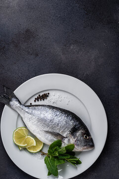 Raw fifh dorada with lime slices, seasoning, and mint herb ready for cooking, directly above