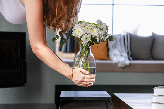 Woman puts vase with bouquet of flowers on table at home